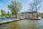 Een paviljoen aan het water met een terras en steiger op een zonnige dag.